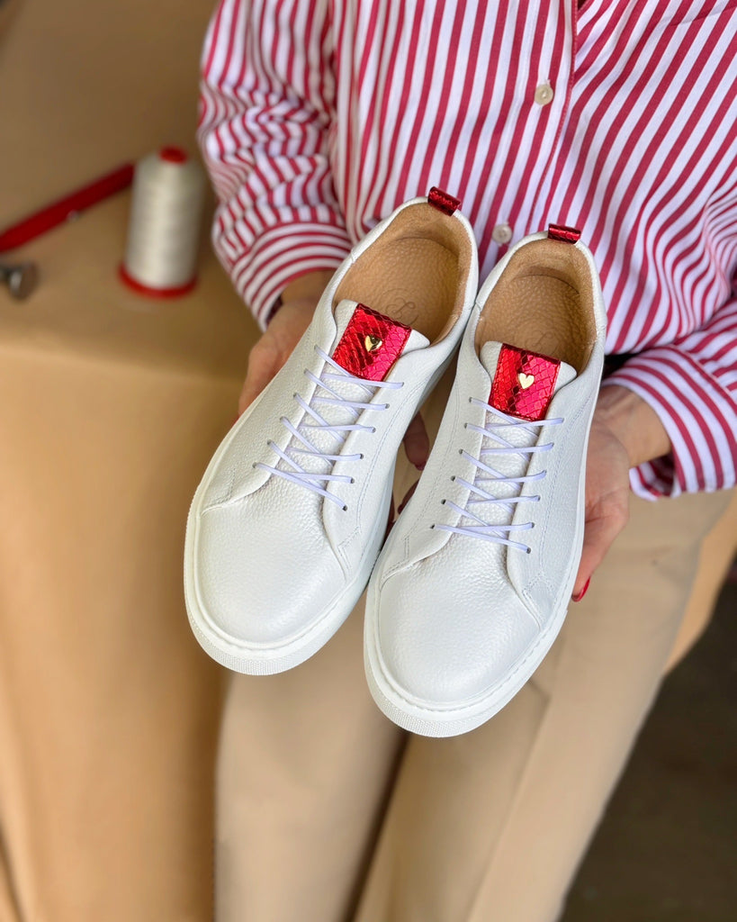White sneakers with red heart details held by a person wearing a red and white striped shirt.